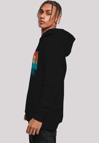 Black hoodie featuring a colorful mountain graphic with sunset hues, soft fabric, long sleeves, and a front pocket.