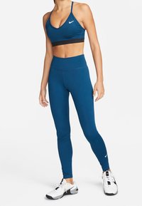 Blauwe sportbeha met zwarte band en bijpassende hoge taille legging. Materiaal is rekbaar, strakke pasvorm. Zwart Nike-logo op beide stukken.