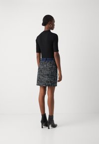 Haut noir ajusté à manches courtes associé à une jupe texturée bleu marine avec un motif multicolore. Le mannequin porte des bottines noires.