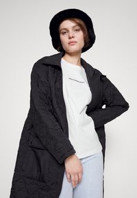 Black quilted jacket with a zip closure, featuring a collar and side pockets, paired with a white crew neck t-shirt and light denim jeans.