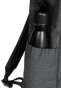 Borraccia nera parzialmente visibile in una tasca laterale di uno zaino grigio scuro e texture, dotato di spallacci regolabili.