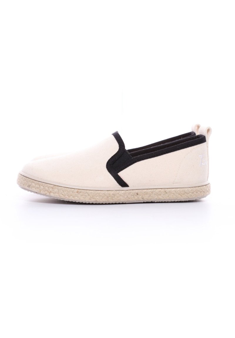 Chaussure slip-on en toile beige avec des accents noirs, dotée d'une semelle en jute tressé et de panneaux élastiques de chaque côté pour un enfilage facile.