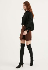 Maglione nero cropped a maglia con maniche a volant abbinato a una gonna marrone a vita alta con spacco e stivali neri con tacco alti fino al ginocchio.