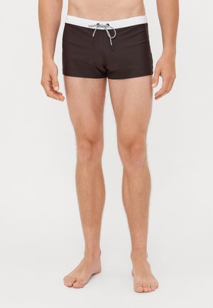 Braune Badehose mit einem weißen elastischen Bund und schwarzem Kordelzug, die einen engen Sitz und einen glatten, leichten Stoff aufweist.