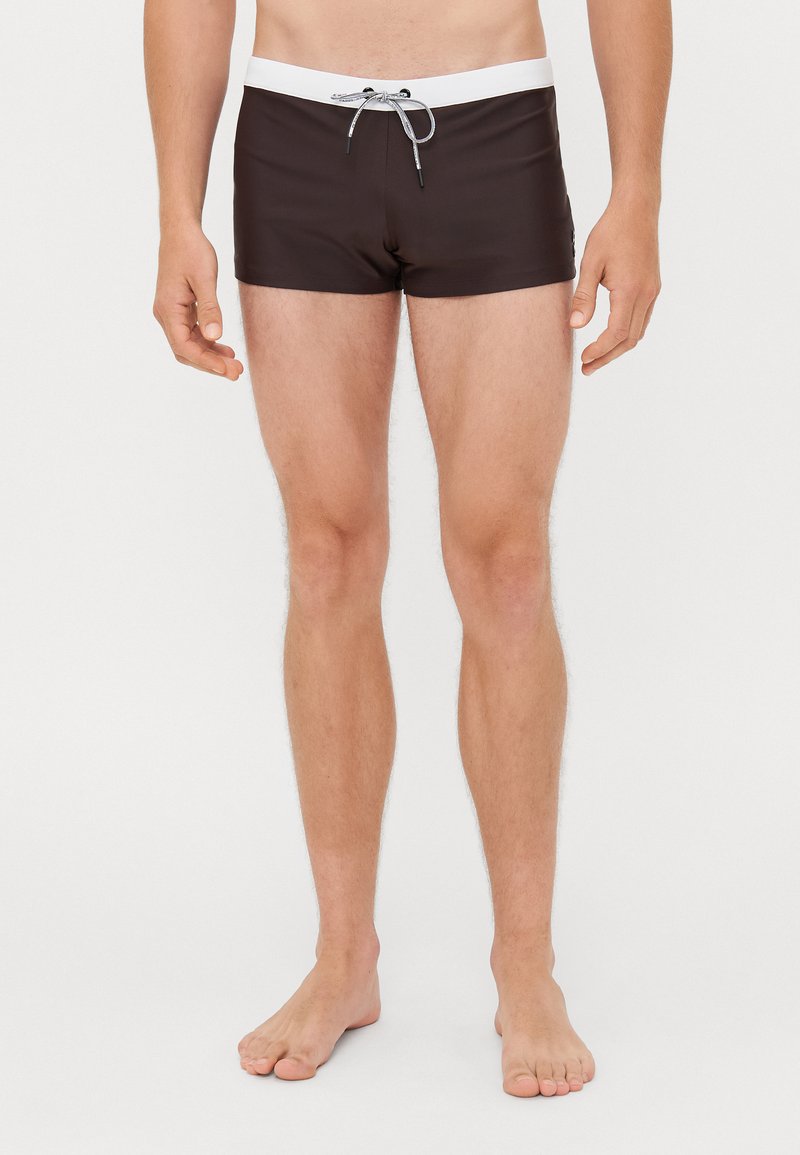 Costume de baie maro cu un brad elastic alb și șnur negru, având o potrivire strânsă și un material neted, ușor.