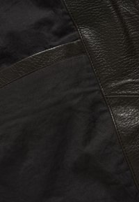 Pannelli in pelle marrone scuro e tessuto morbido cuciti insieme, mostrando texture e cuciture a contrasto in primo piano.