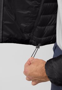 Veste matelassée noire avec un extérieur lisse et une isolation intérieure. Réglage par cordon à l'ourlet, avec un sujet et des tirettes texturées.