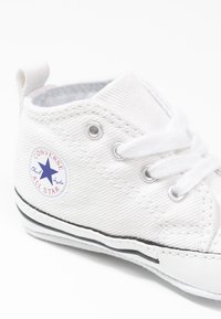 Białe wysokie trampki z płótna z metalowymi oczkami, białymi sznurówkami, czarną gumową podeszwą i niebieskim logo gwiazdy z boku. Teksturowany materiał o delikatnym prążkowaniu.