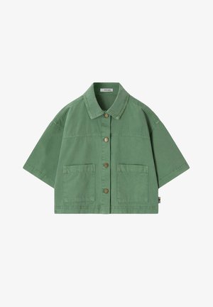 Lunettes de soleil marron en forme de cœur suspendues à la poche avant d'une chemise vert clair à boutons.