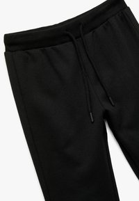 Zwarte joggingsbroek gemaakt van zachte stof, met een elastische tailleband, verstelbaar trekkoord en taps toelopende benen. Glad oppervlak gedurende de hele broek.
