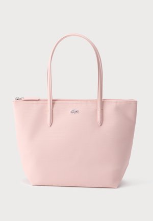 Sac cabas rose clair avec deux longues anses, fermeture zippée, et un petit logo crocodile argenté au centre devant.