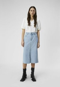 Jupe midi en denim bleu clair avec fente à l'avant, taille haute et cinq poches. Assortie à un haut blanc à col en V et manches bouffantes, ainsi qu'à des bottines noires.