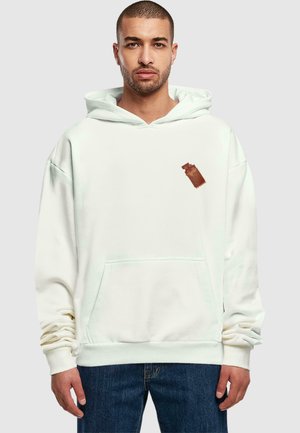 White hoodie made of soft fabric features a kangaroo pocket and a brown patch design. The sleeves are slightly oversized for a relaxed fit.