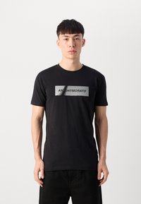 Black cotton t-shirt featuring a rectangular graphic in silver with the text "ANONYMOUS." Classic fit with short sleeves and round neck.