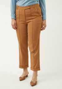 Brune bukser med skræddersyet pasform, der har sidelommer, lodrette sømme og opkrøllede manchetter. Bæres med brune slip-ons dekoreret med accenter.