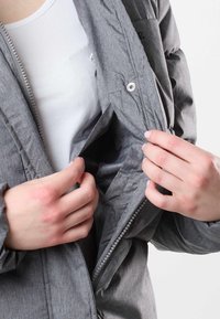 Gray insulated jacket with a zip closure and snap details. Interior pocket is visible. The fabric has a textured finish and a subtle pattern.