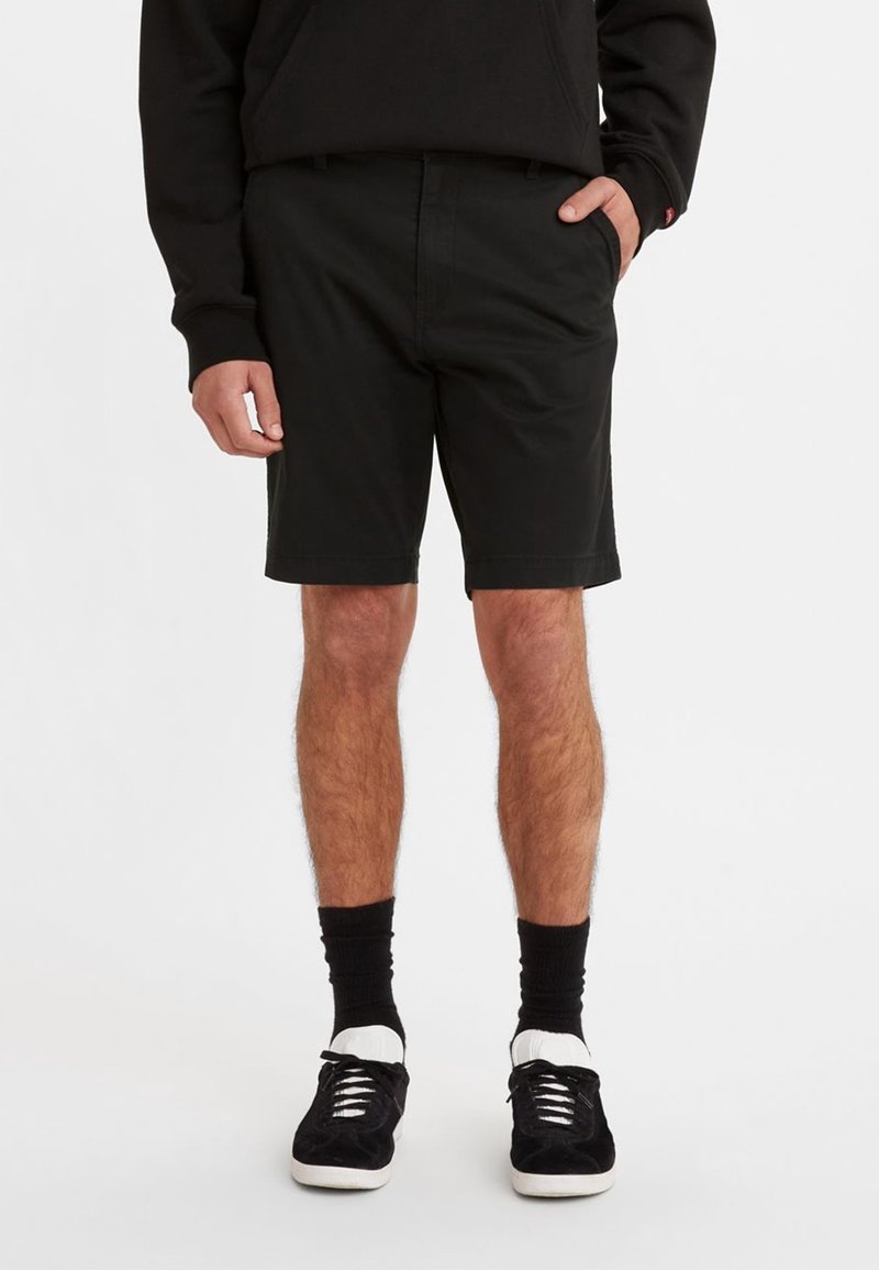 Shorts noirs en coton à coupe droite, avec poches latérales et sans détails, assortis à des baskets noires et des chaussettes montantes noires.