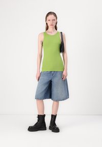 Green sleeveless top, denim shorts, and black lace-up ankle boots. The shorts are loose-fitting with a frayed hem. A small black bag is worn.
