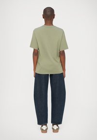 Camiseta de algodón verde olivo con un corte relajado, combinada con jeans de pierna ancha azul oscuro y zapatillas marrones con acentos verdes.