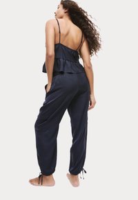 Conjunto de loungewear de dos piezas en azul marino que incluye una camiseta sin mangas con volantes y tirantes finos, y pantalones holgados con puños elásticos y bolsillos.