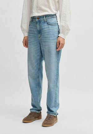 Lichtblauwe high-waisted jeans met een losse pasvorm, voorzien van subtiele vervaging en een vijf-vakken ontwerp. Gecombineerd met bruine suède sneakers.
