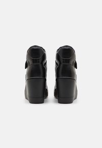 Botas de cuero negro de tacón alto con textura suave, punta redonda y una hebilla visible en la parte trasera. Diseño de tacón en cuña.