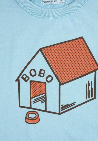 Chemise bleu clair avec illustration d'une niche étiquetée "BOBO" en marron et orange, avec une gamelle devant.