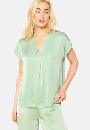 Lichtgroene zijden blouse met een v-hals en kapmouwen, voorzien van een losse pasvorm en een plooidetail aan de voorkant. Gladde textuur en zachte glans.