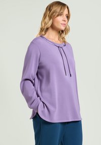 Felpa pullover lilla con scollo rotondo, chiusura con cordino, maniche lunghe e vestibilità comoda, abbinata a pantaloni blu navy.