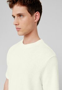 T-shirt en tricot blanc avec un col rond et des manches courtes, arborant un motif texturé sur le tissu, mettant en avant un design respirant.