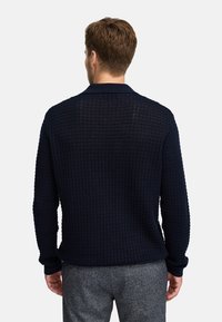 Granatowy sweter o fakturze z wzorem w kratkę, z kołnierzykiem i długimi rękawami, w zestawie z szarymi spodniami.