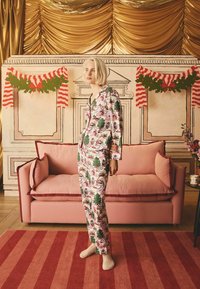 Božične pižame imajo rožnato ozadje z zelenimi drevesi, vintage okraski in belimi poudarki. Dopolnjuje jih mehka rožnata sedežna garnitura.