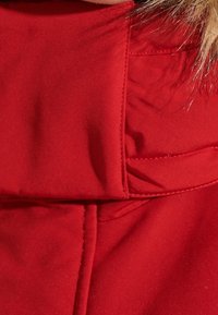 Rode stof met een gladde textuur heeft een omslagdetail bij de halslijn en een zichtbaar stiksels patroon langs de randen.