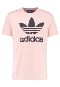 T-shirt en coton rose clair avec un grand logo Adidas noir comprenant trois bandes et un graphique en trèfle sur le devant. Manches courtes.
