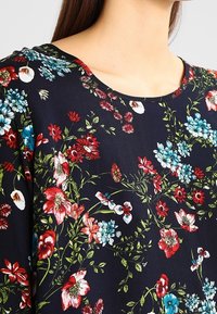 Top con motivo floreale su sfondo blu navy, caratterizzato da fiori rossi e blu. Tessuto morbido e scollatura tonda.