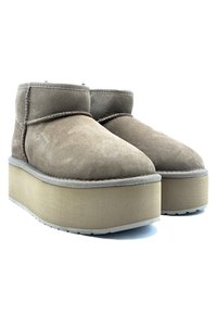 Stivaletti in suede marrone con una robusta suola piatta beige, punta arrotondata e dettagli cuciti lungo le cuciture. Suola in gomma per una buona aderenza.