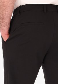 Pantaloni neri su misura con una texture liscia, vestibilità slim e una tasca posteriore. Linee pulite e dettagli di design minimalisti visibili.