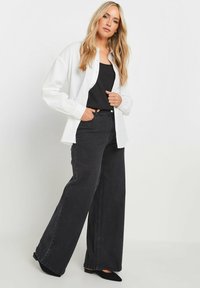 Camicia bianca a maniche lunghe sopra un top nero, abbinata a pantaloni neri a vita alta e gamba larga e ballerine nere. Tessuto morbido e vestibilità comoda.