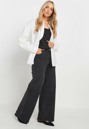 Chemise blanche boutonnée sur un débardeur noir, associée à un jean noir taille haute à jambes larges et des ballerines noires. Tissu lisse et coupe décontractée.