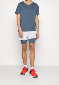 Pánský sportovní outfit s krátkým rukávem, tmavě modrá košile, bílé šortky s tmavě modrými akcenty a černorudé tenisky. Hladká tkanina, moderní střih.