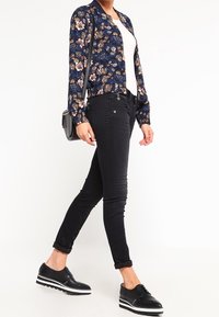 Blus med blommönster i marinblått, vit linne under, svarta skinny jeans och svarta skor med vita sålar. Enkel axelremsväska.