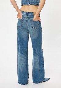 Pantalones vaqueros de mezclilla azul de pierna ancha con un lavado desgastado, que cuentan con una cintura alta, dos bolsillos traseros y un sutil desgaste cerca del dobladillo.