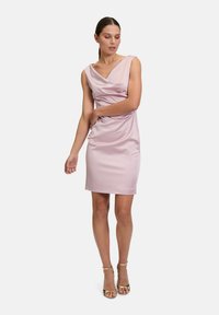 Abito da cocktail in satin rosato, con scollatura drappeggiata e silhouette aderente, caratterizzato da una texture liscia e un orlo che arriva al ginocchio.