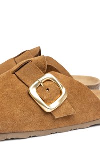 Le ciabatte slip-on in suede marrone presentano un ampio dettaglio con fibbia, una consistenza morbida e una soletta sagomata. La suola ha un leggero motivo di battistrada.