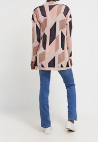 Stickad cardigan i rosa, beige och marinblå geometriska mönster, med en lång, lös design, rund hals och ribbad kant.