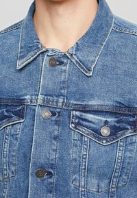 Ljusblå denimjacka med klassisk krage, knäppning fram, fickor och synliga sömnadsdetaljer. Texturerad tyg.