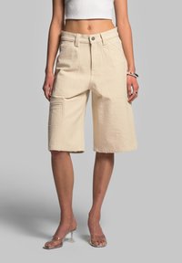 Shorts in denim beige con vita alta, con dettagli delle tasche cuciti e orlo grezzo. Realizzati in tessuto testurizzato, design di lunghezza al ginocchio.