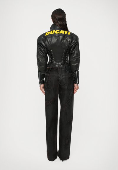 Jachetă din piele neagră cu logo-ul galben "DUCATI", cu un design împletit pe spate. Asortată cu pantaloni largi negri, cu un model texturat subtil.
