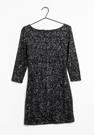 Vestido corto negro de manga larga con lentejuelas y escote bote colgado en una percha negra sobre un fondo blanco.