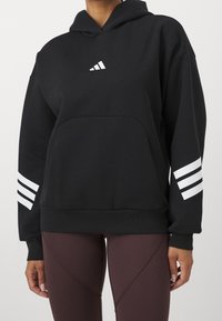 Czarna bluza z kapturem, z przednią kieszenią typu kangur i białymi, trzema paskami na rękawach. Wykonana z teksturowanej tkaniny.
